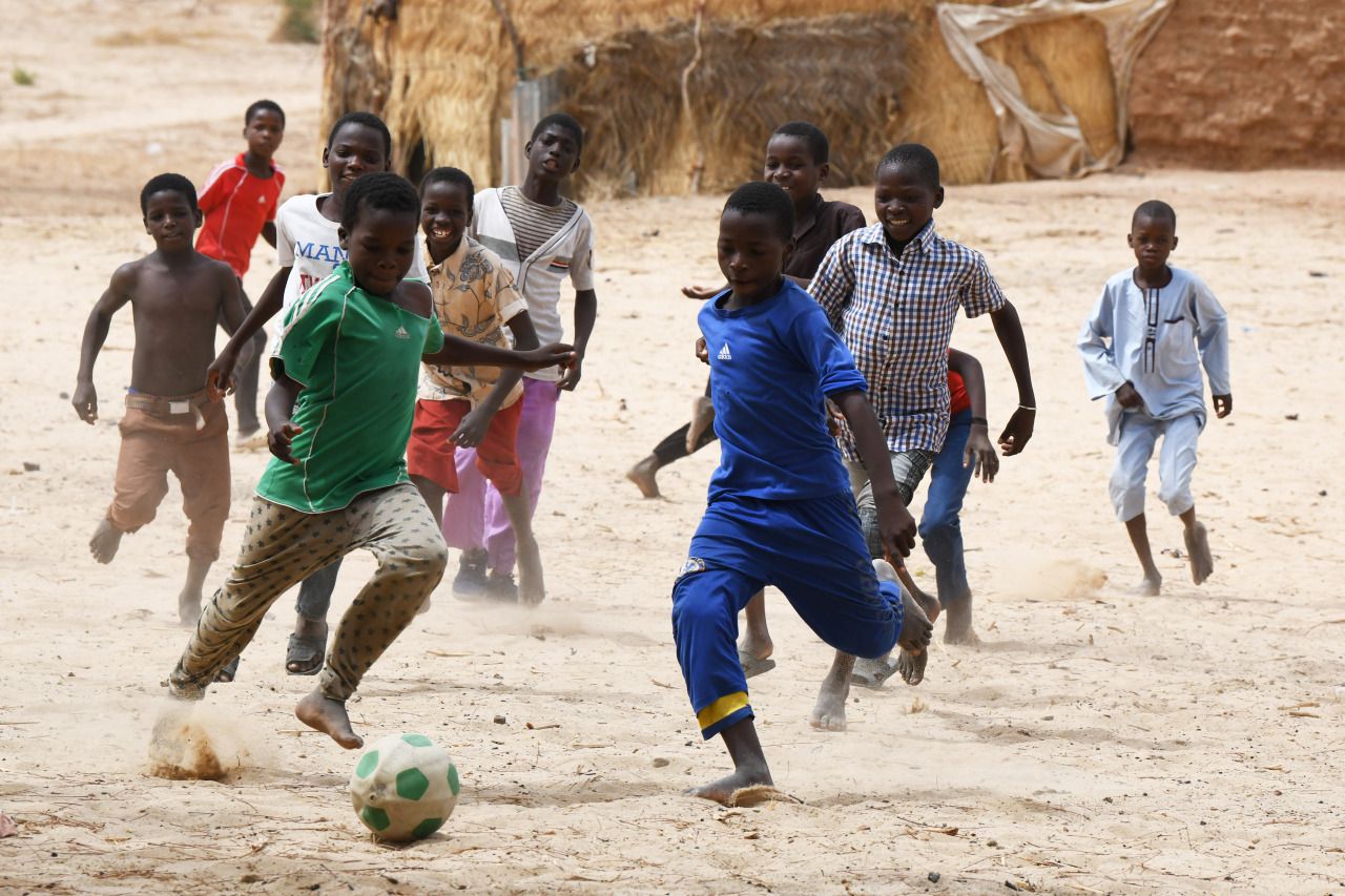 Children playing football together on a dirt pitch